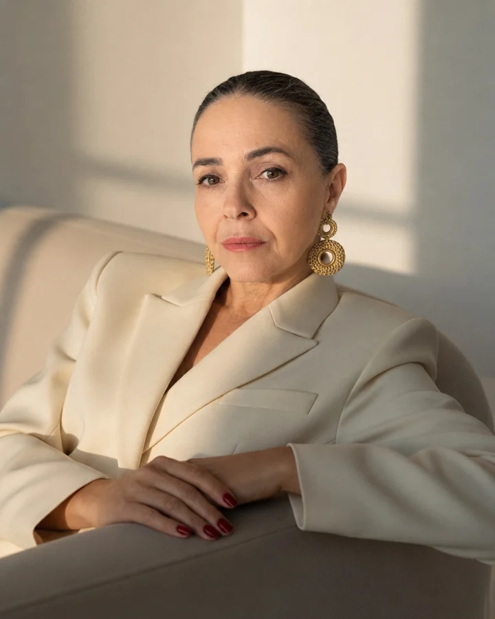 Retrato de Nani Vicente, professora do Clube Criadores de Conteúdo, sentada em uma poltrona clara usando blazer off-white